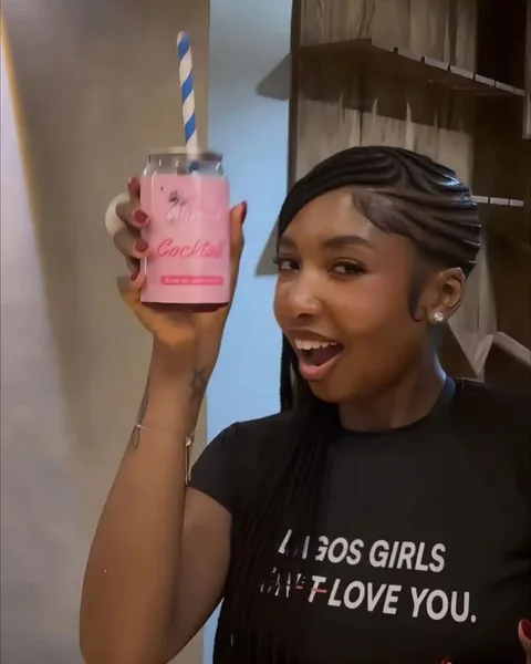 A woman with braids holds a pink Brightside can up to take a sip.