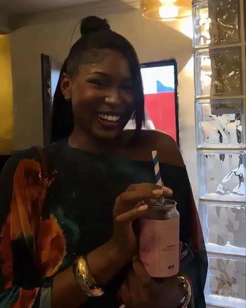 A smiling woman holds a pink Brightside can with both hands.